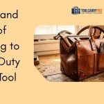 A rich brown full-grain leather tool bag filled with a hammer, pliers, and screwdrivers, placed on a rustic wooden workbench in a workshop setting, with a horsehair cleaning brush and a tin of natural leather conditioner beside it.