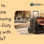 A heavy-duty black rolling tool bag with large all-terrain wheels, open wide-mouth top showing an organized orange interior filled with wrenches, screwdrivers and power tools, sitting on a construction site with workers and equipment in the background — ToolCarryPro
